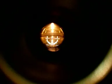 A close-up of a spherical, illuminated clock at night, displaying the words 'WUNSCH ZEIT VERTRAUEN' (Wish Time Trust). The warm light from the clock contrasts with the dark surroundings, creating a soft glow.